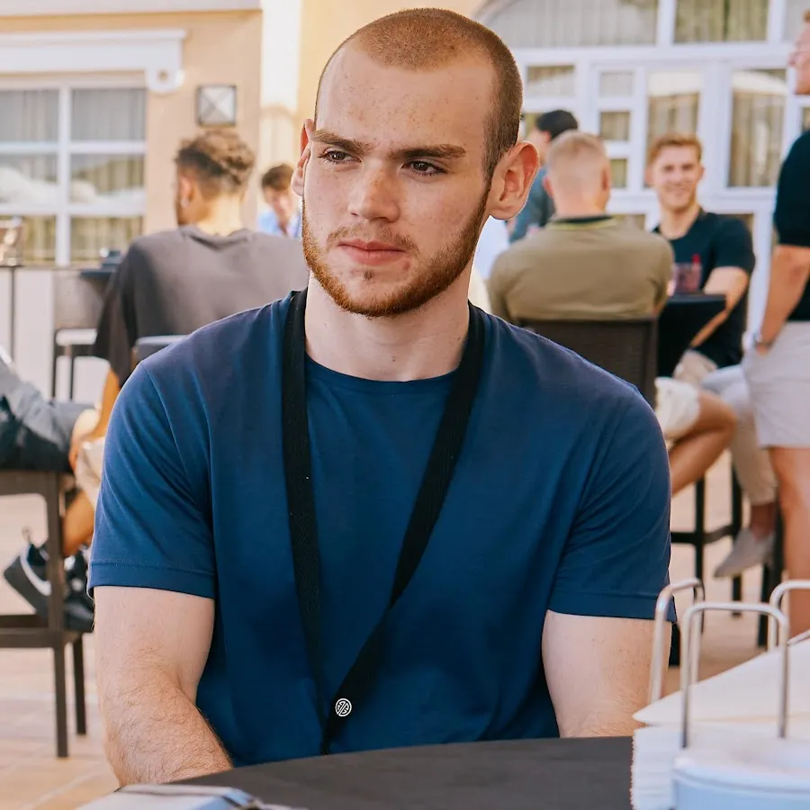 Mongraal sitting in a chair with a blue t-shirt and people sitting behind him