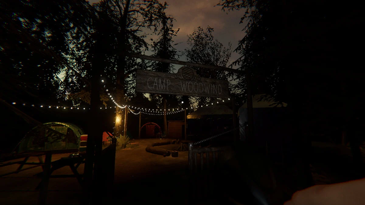 A wooden sign that says Camp Woodwind hanging over a wooden gate and a camp area with lit up string lights behind it in Phasmophobia.